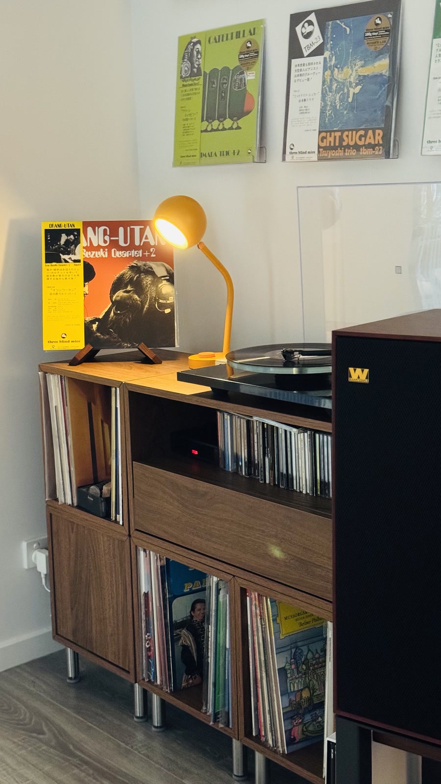 My listening corner: a Rega turntable on a walnut cabinet of records and CDs, a Wharfedale speaker, an orange desk lamp, and Three Blind Mice LPs on the wall and on a stand.